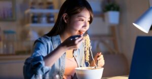 (woman eating ramen at her computer)