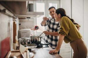 (man spoonfeeding a woman what he just cooked)